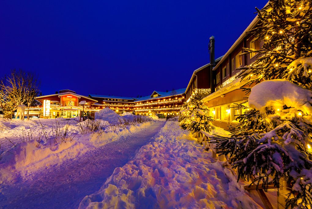 Snow covered village buildings illuminated at night with warm glowing lights creating a cozy winter atmosphere. Levi, Lapland.