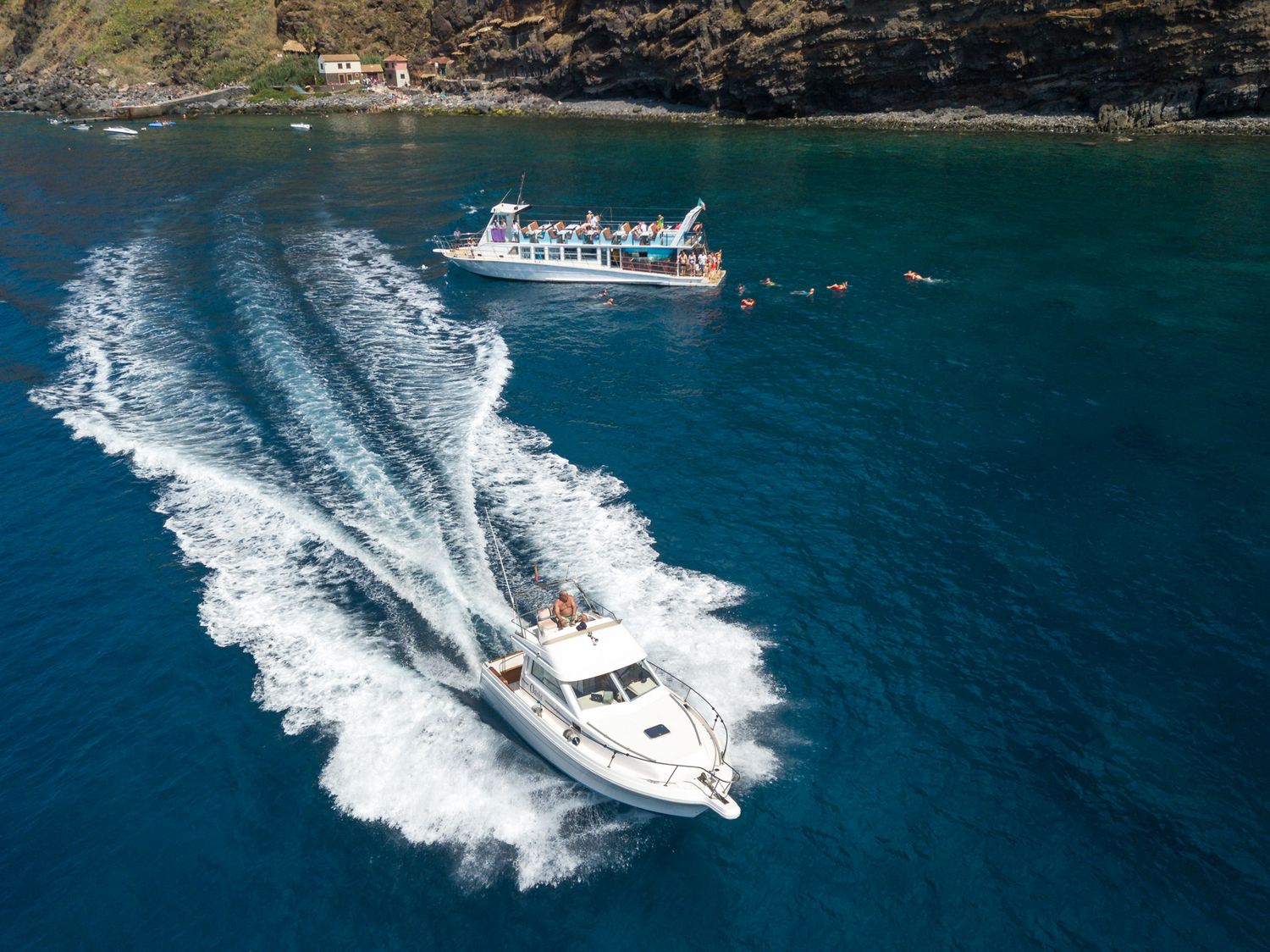 Aerial view of luxury boats creating white wakes while cruising through turquoise tropical waters.