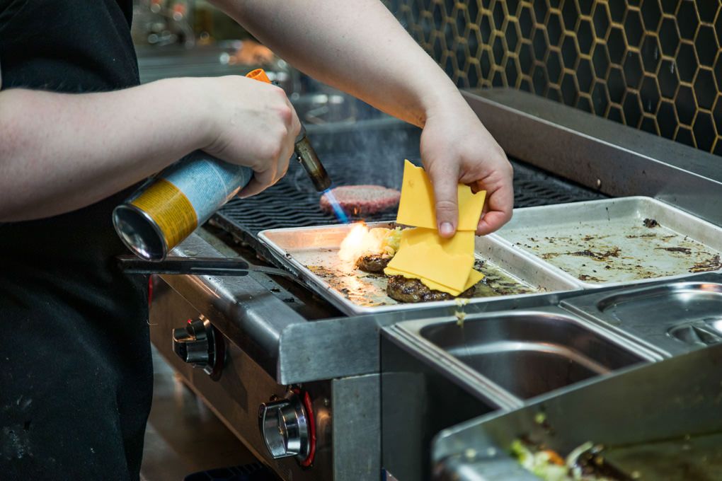 A person grilling food on a flat top griddle while using spatulas to prepare multiple items simultaneously. Le Kok, Iceland.