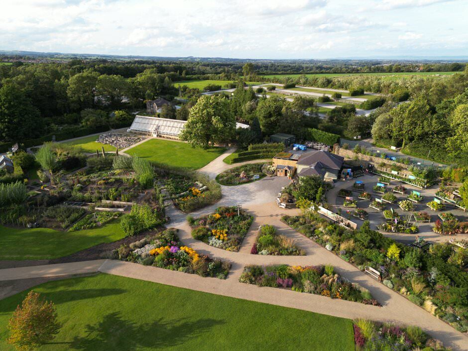 Aerial view of a beautifully landscaped garden park with winding paths, flower beds and green spaces in a rural setting.