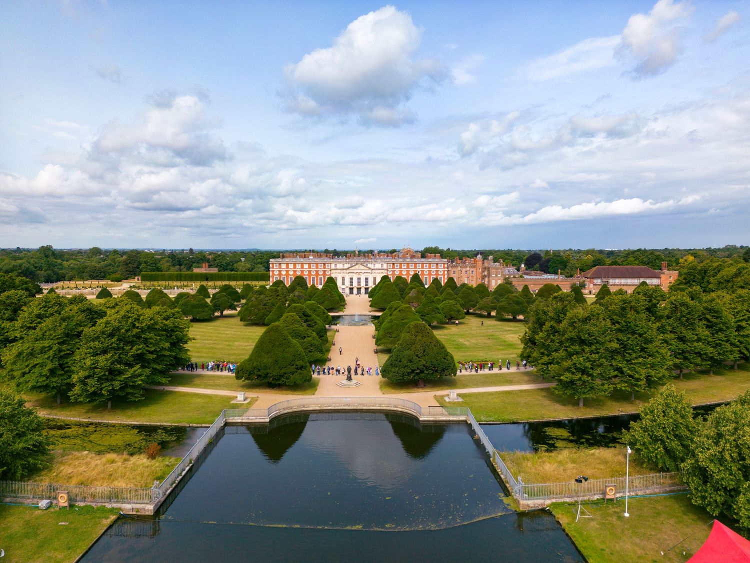 Aerial drone photograph of Hampton Court Palace featuring formal gardens, tree-lined avenues and ornamental water features.