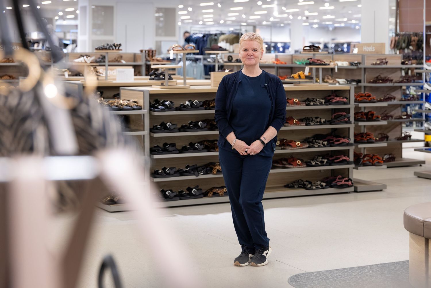 Woman in navy outfit stands confidently in a modern shoe department store with shelves of footwear displays.