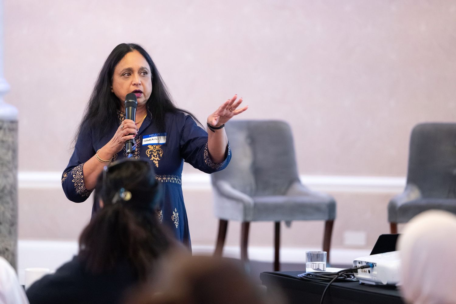 Woman speaker gestures passionately while holding microphone at indoor conference event.
