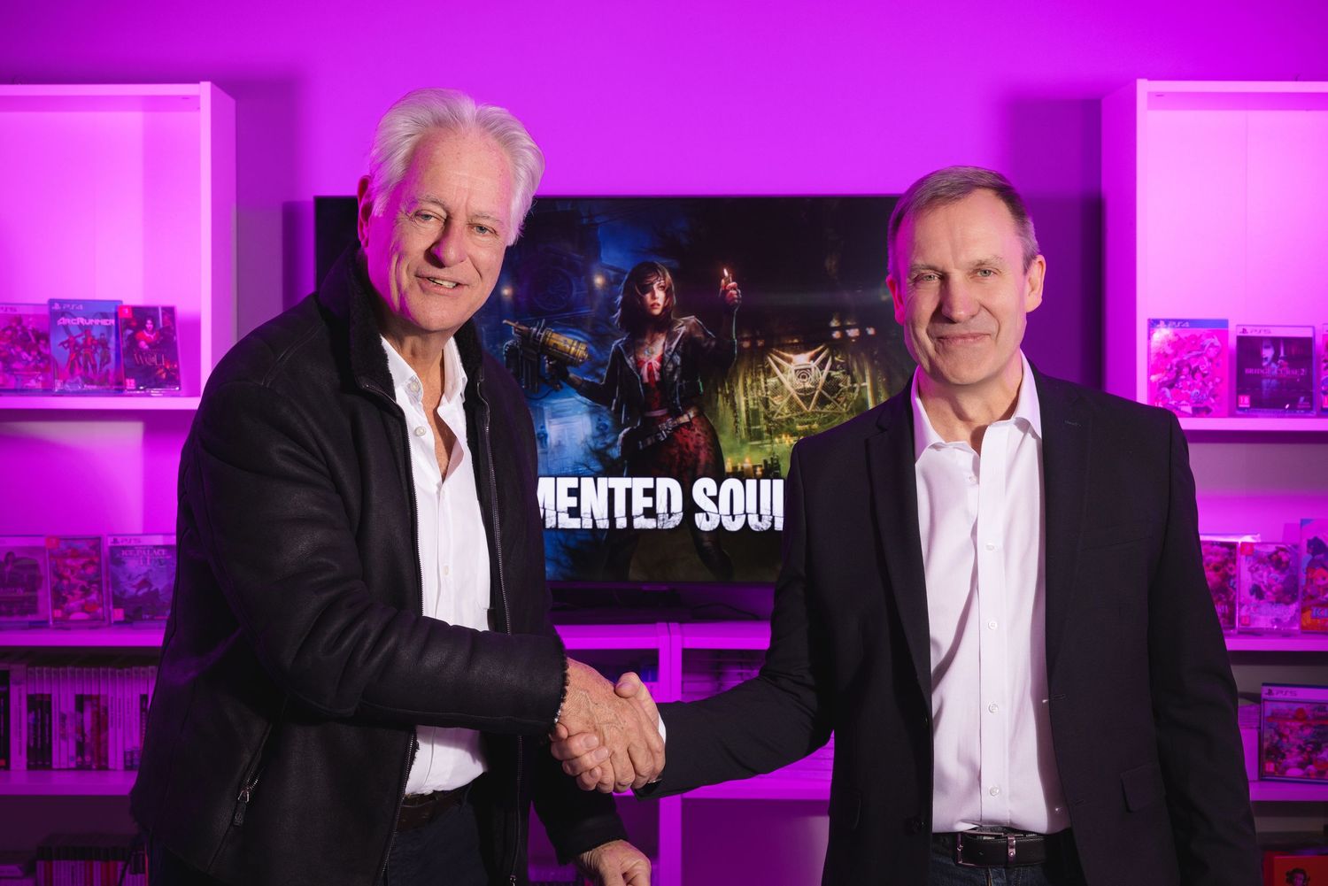 Two men shaking hands in front of a gaming display with purple lighting and Tormented Souls game artwork.