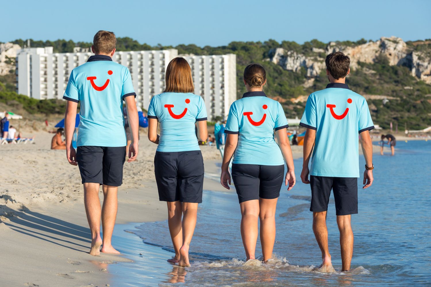 Four TUI staff walk along the beach showing off the TUI Smile logo on their uniform