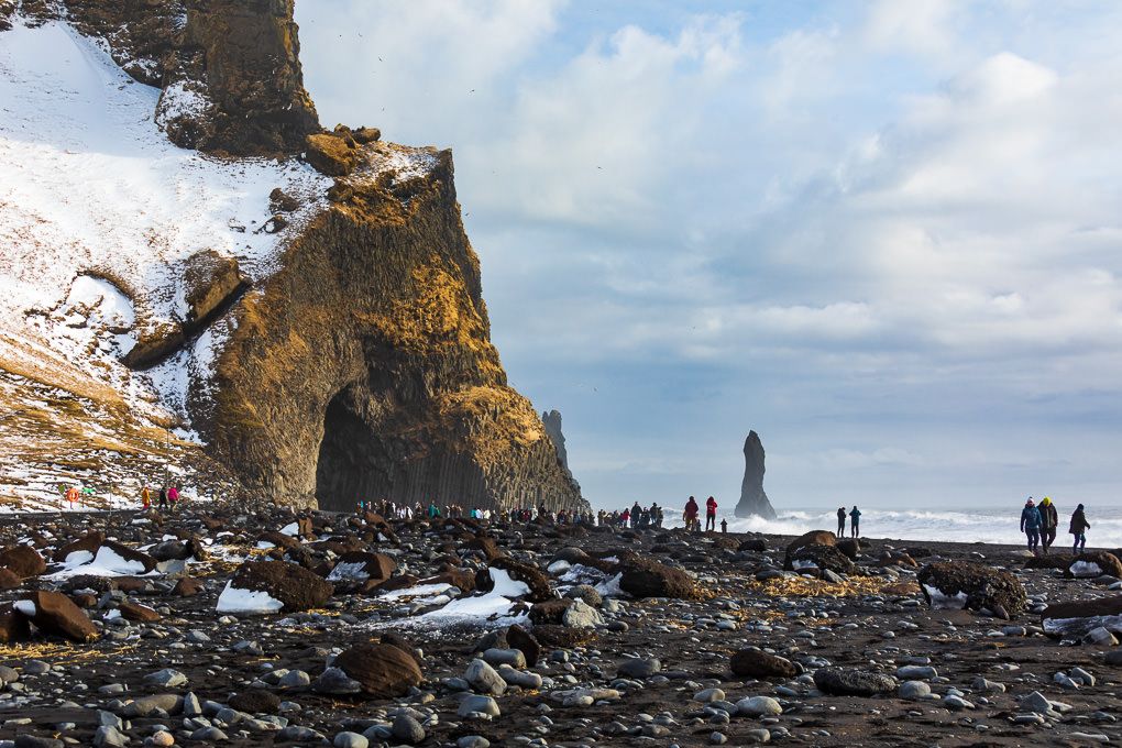 Silhouettes of people exploring Reynisfjara Black Sand Beach and towering cliffs in Iceland.