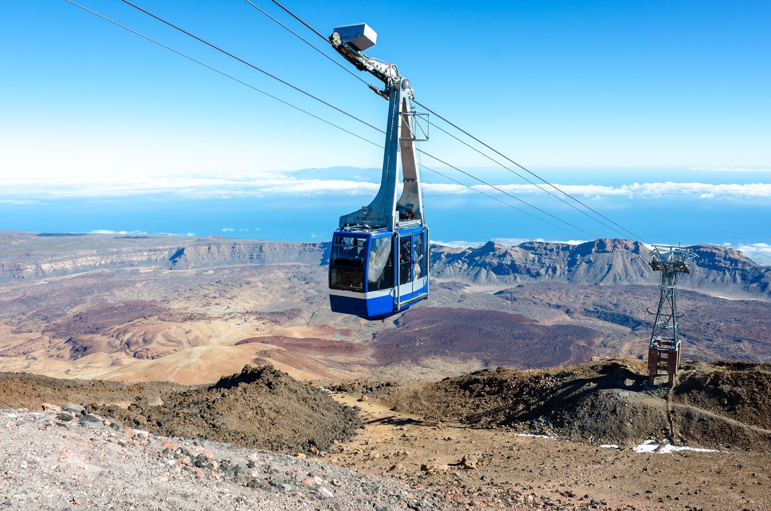 Blue cable car gondola ascending Mount Teide in Tenerife with dramatic volcanic landscape and ocean views below.