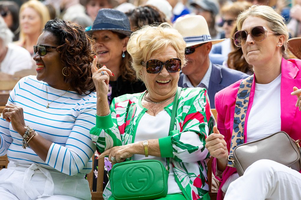 A crowd of people wearing colourful clothing and sunglasses gather together at the RHS Chelsea Flower Show.