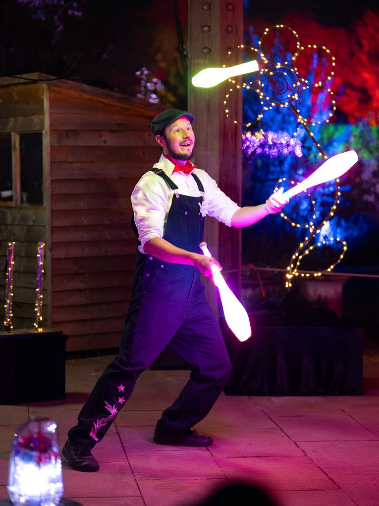 Performer juggling glowing LED light sticks during the illuminated show at Glow at RHS Bridgewater, set against colourful nighttime lights.
