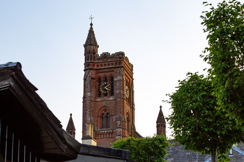 The historic red-brick church tower of Moffat rises against the blue sky, with green trees framing its Gothic architecture.