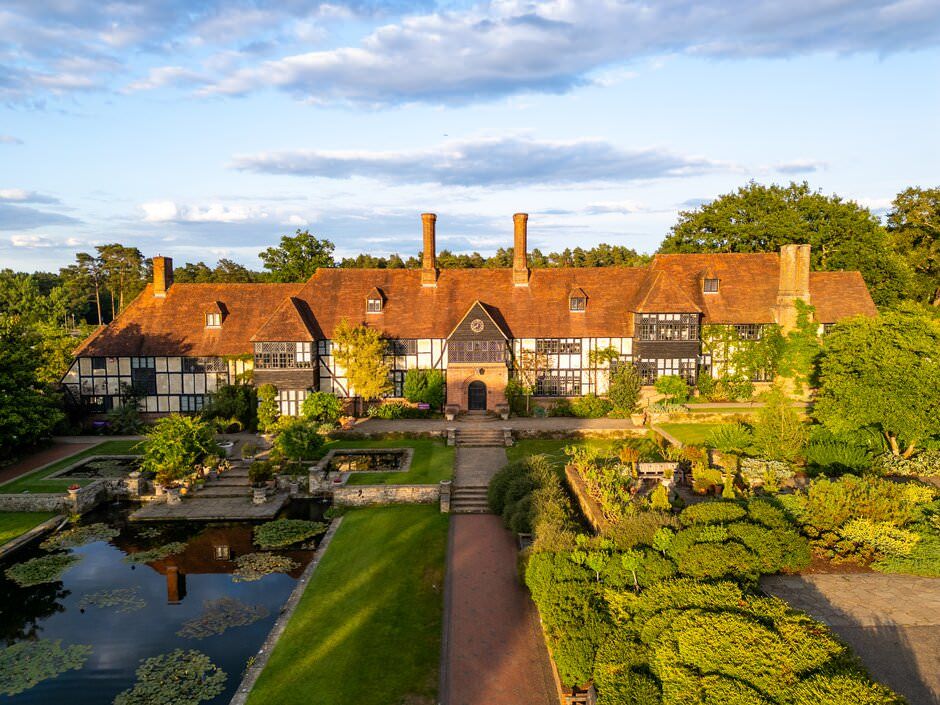 Aerial view of a historic Tudor-style mansion with manicured gardens, reflecting pools and stone pathways in England.