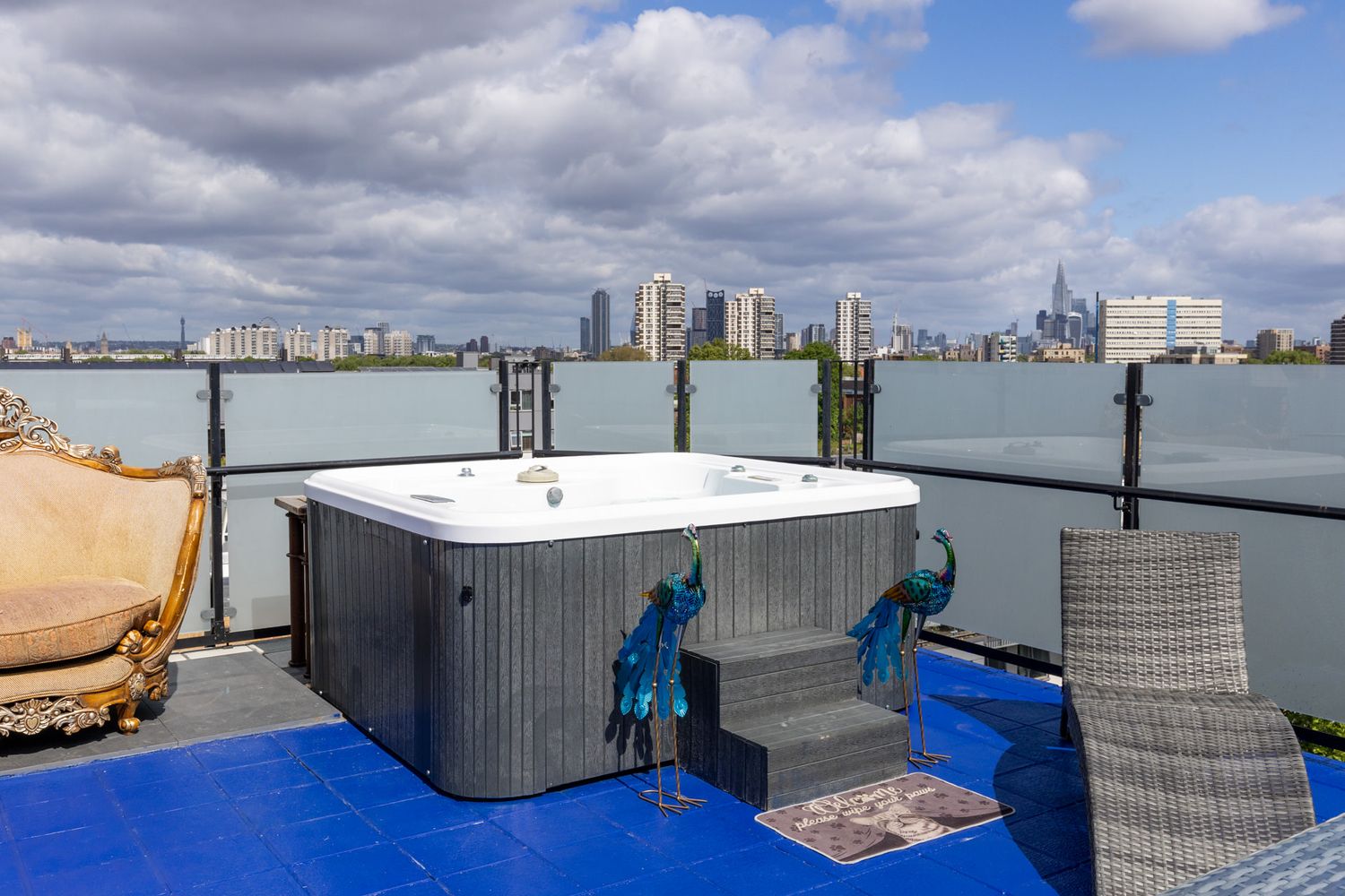 Rooftop hot tub overlooking Detroit city skyline and river with modern patio furniture on blue deck flooring.