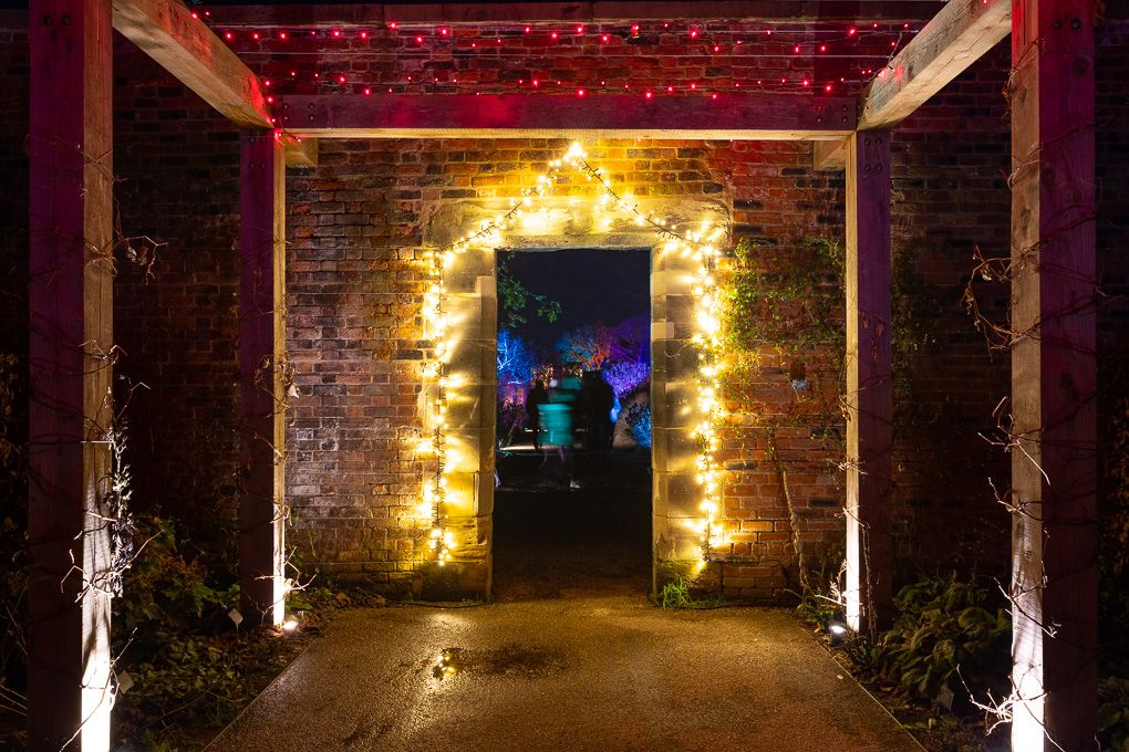 String lights illuminating a rustic brick archway at night during the Glow event at RHS Bridgewater, creating a warm, glowing tunnel effect.