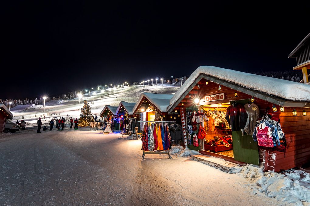 A row of rustic log cabins decorated with warm glowing Christmas lights against a snowy winter landscape in Levi, Lapland. Travel photos.