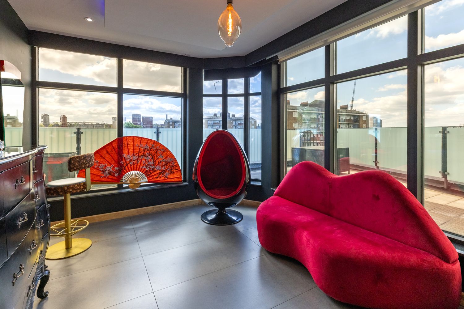 Real estae photography of a modern penthouse in London with large windows and a red curvy sofa seating against city views.