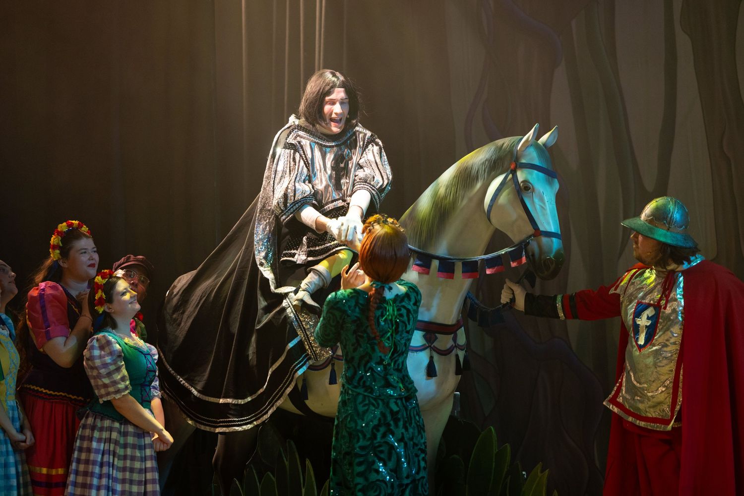 Knight character rides a white horse prop surrounded by fairy tale cast during theatre photography at Castle Theatre Wellingborough