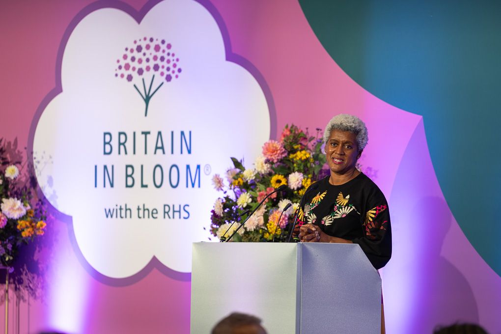 A stage setup with purple lighting and floral displays for the Britain in Bloom awards ceremony.