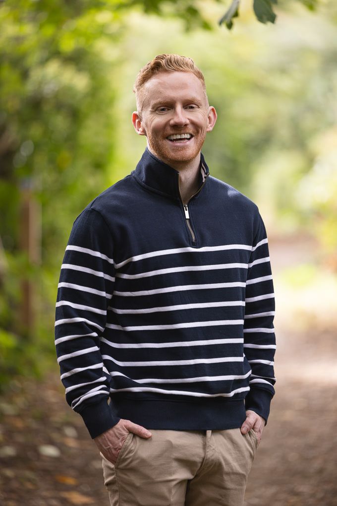 Person in navy and white striped quarter-zip pullover smiling outdoors in natural setting.
