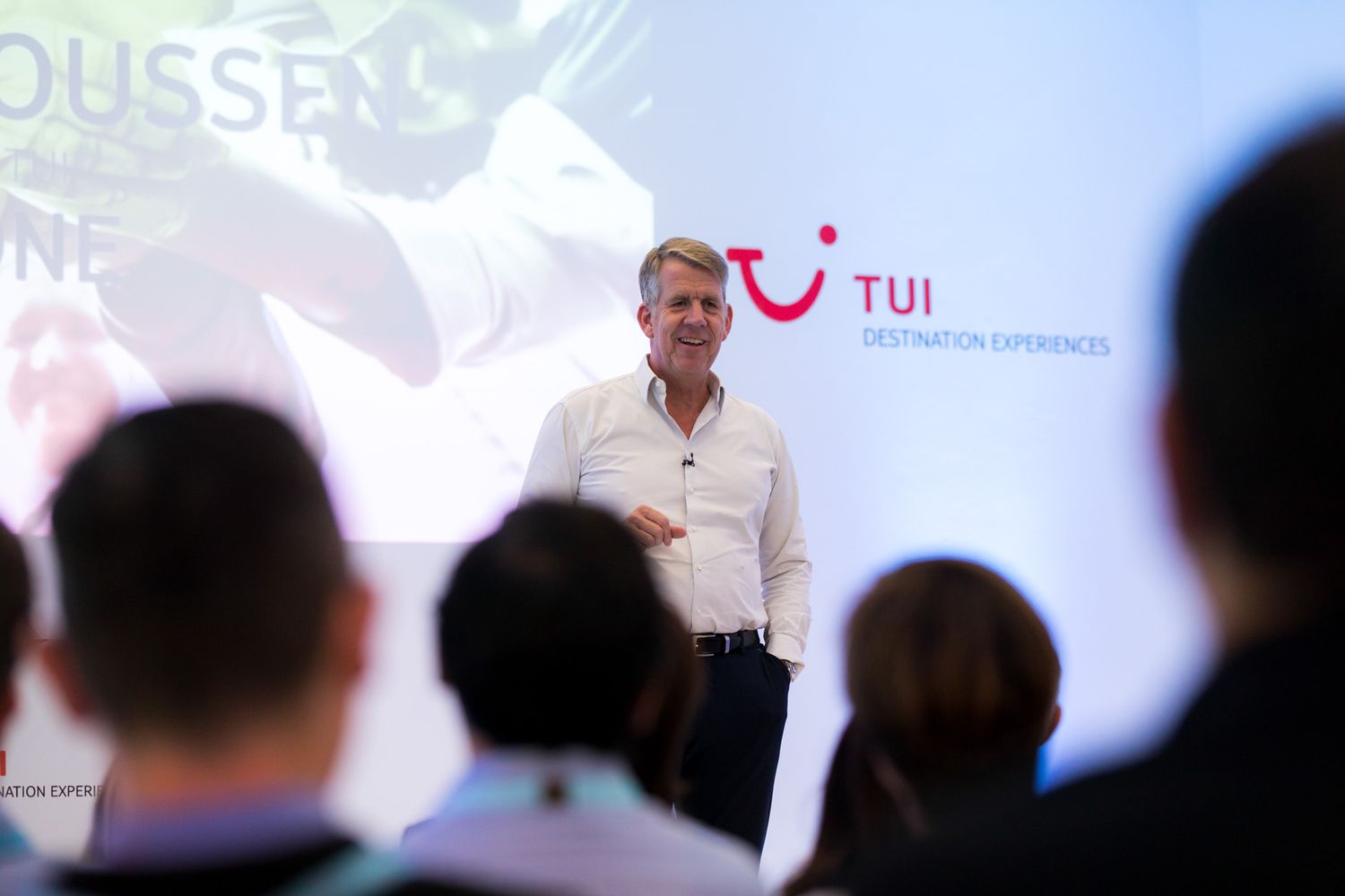 A presenter delivers a business presentation at a TUI travel company corporate event with audience members silhouetted in foreground.