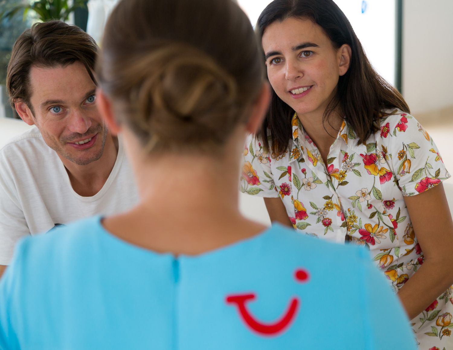Three people having a conversation, with one wearing a colourful floral shirt and another in a TUI light blue uniform with a TUI smile logo.