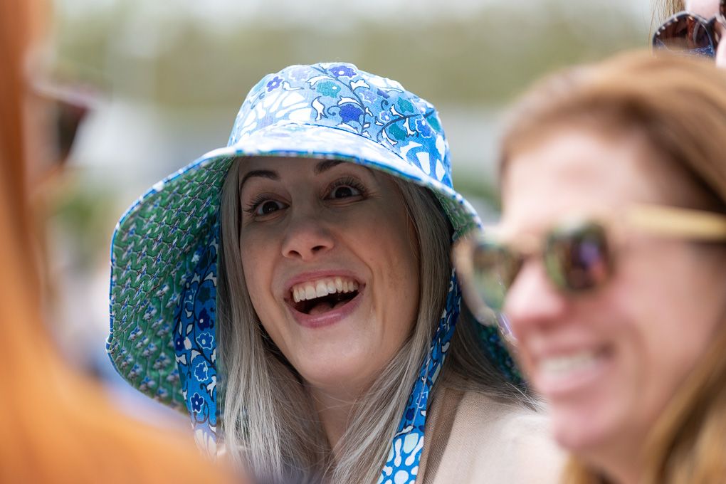 Group of people wearing colorful sun hats laugh and smile together during the Chelsea Flower Show.