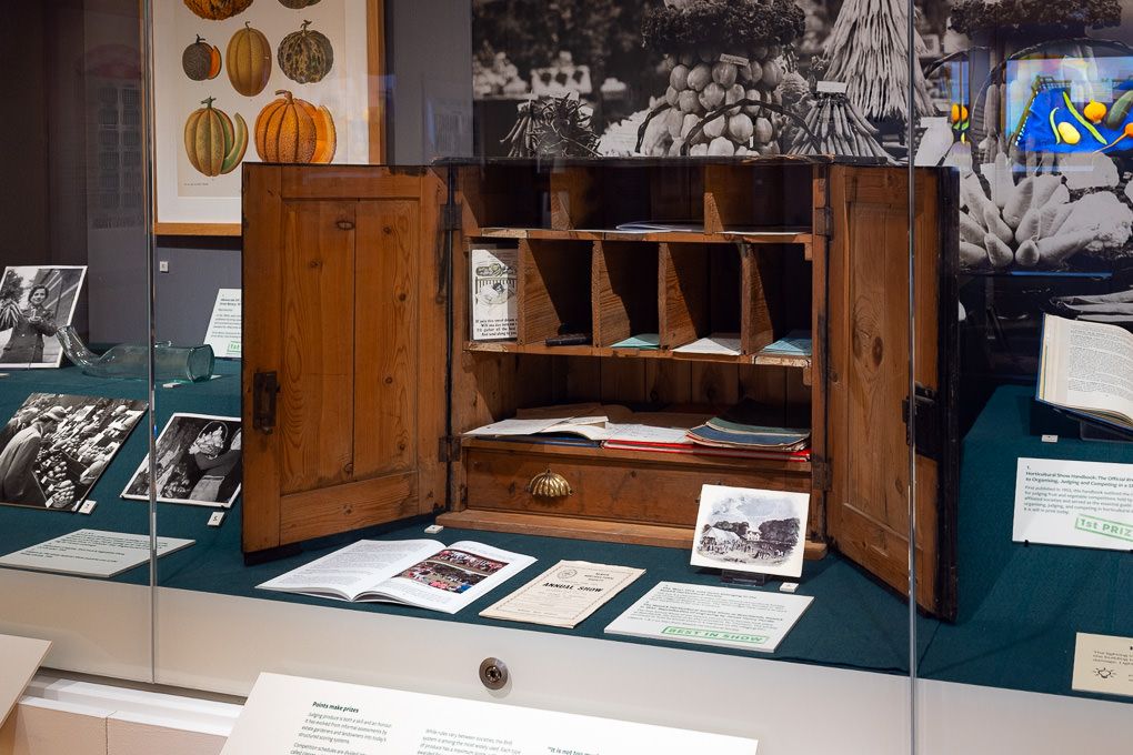 RHS Wisley museum exhibition with a vintage wooden cabinet displaying historic artefacts and documents.