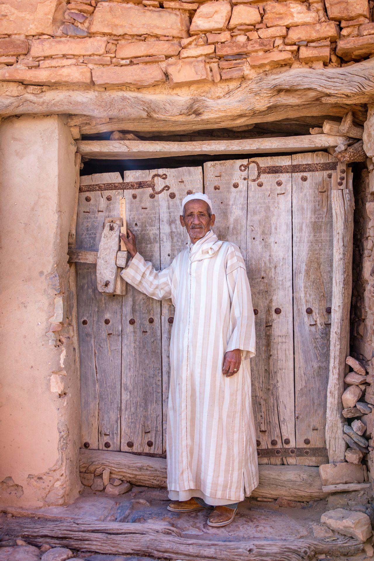 Traditional wooden door in a clay brick building in Morocco with white fabric clothing.