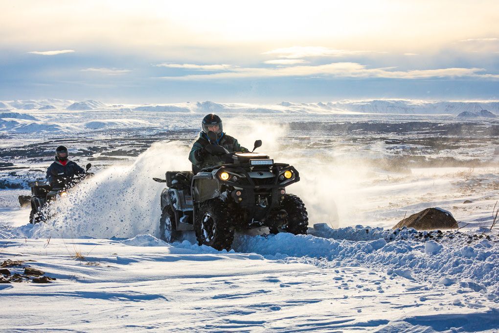 ATV riders racing through snowy terrain kick up powder trails as they speed across a winter landscape at sunset in Iceland. Excursion photo