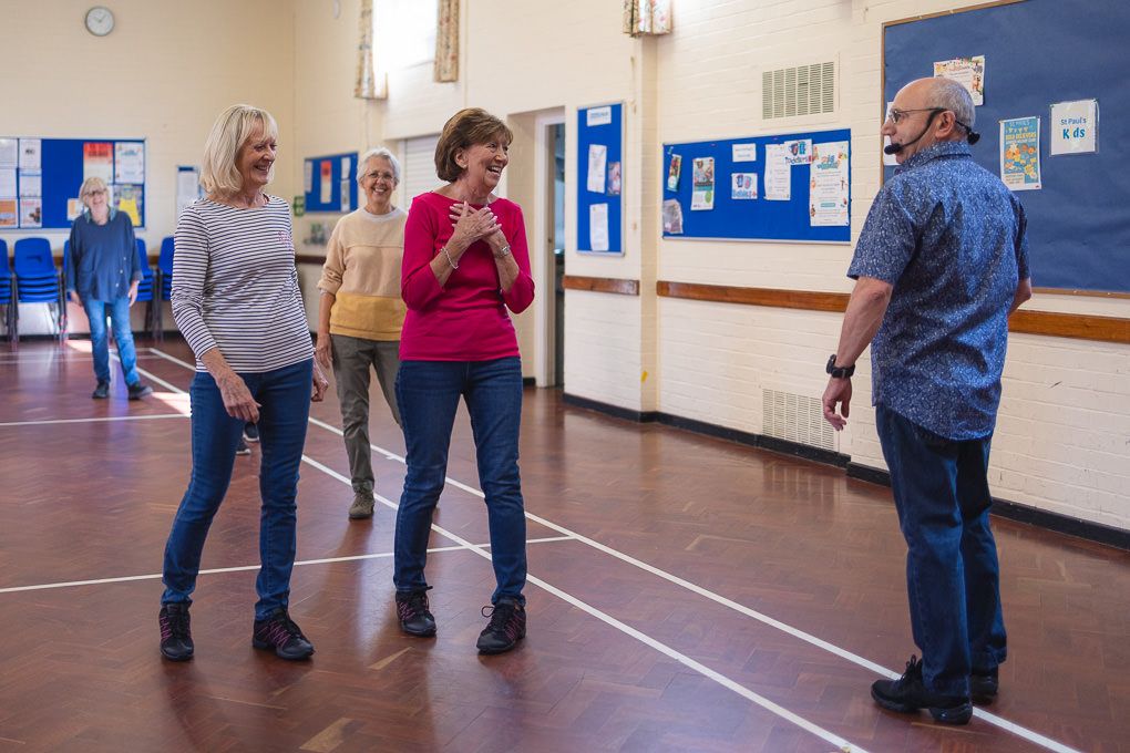 Three people interact and practice dance moves together in a Hertfordshire community centre.