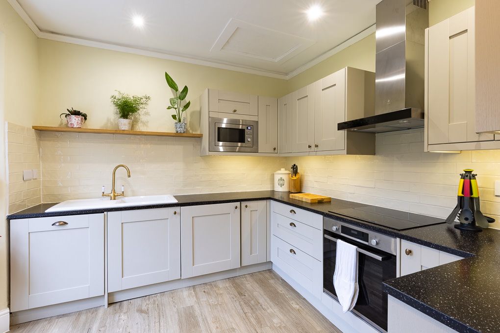 Modern white kitchen with black granite worktops, stainless steel appliances and recessed lighting - interior photography