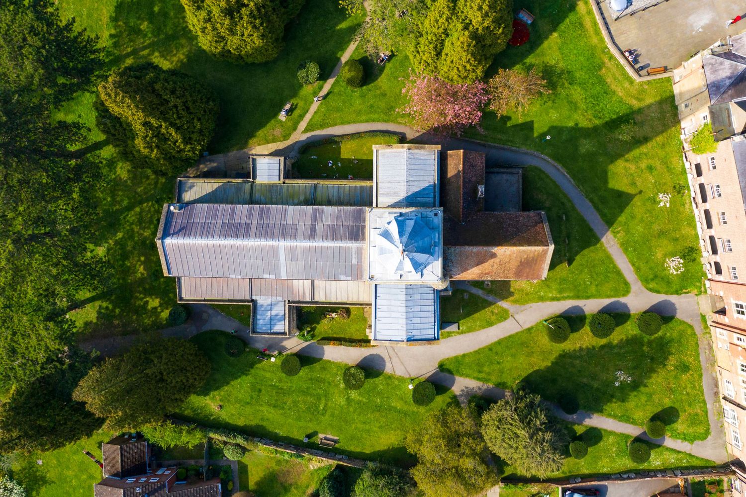 Aerial view of a building with solar panels surrounded by lush green gardens and winding pathways on a sunny day.