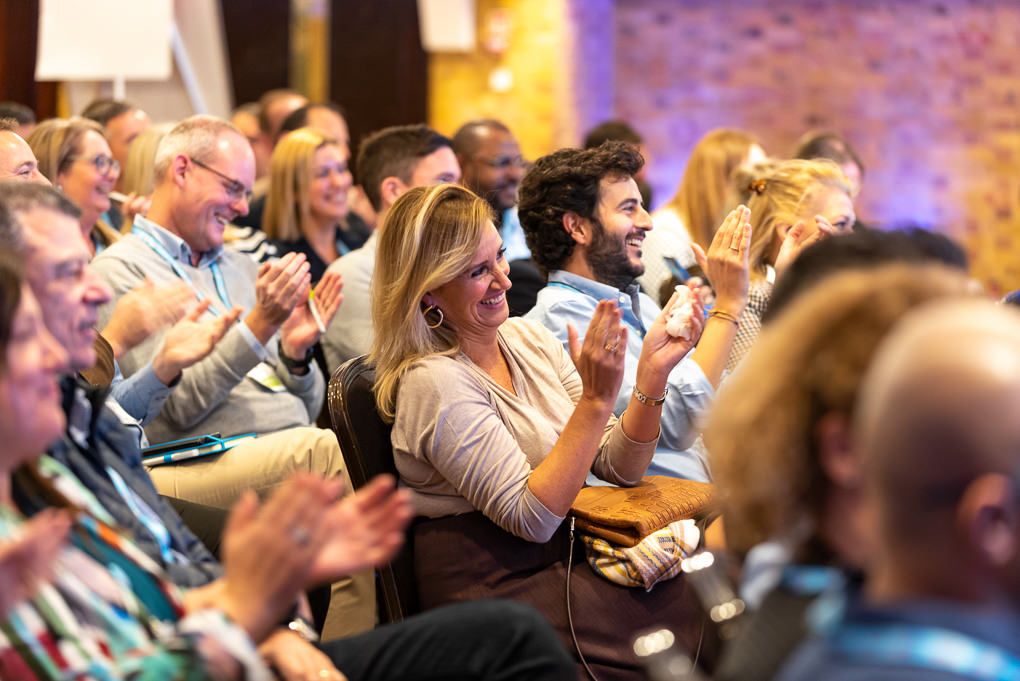 A crowd of enthusiastic audience members applauding and cheering during a live conference event at The Brewery in London.