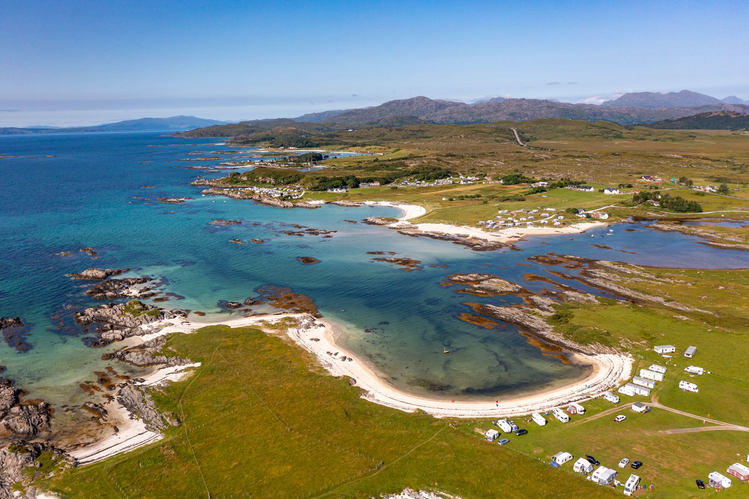 Aerial panorama of rugged coastline with white sandy beaches and turquoise waters along Scottish highlands.
