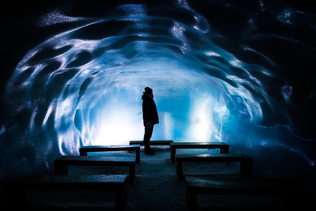 A silhouetted figure stands in a glowing blue ice tunnel at Into the Glacier in Iceland.