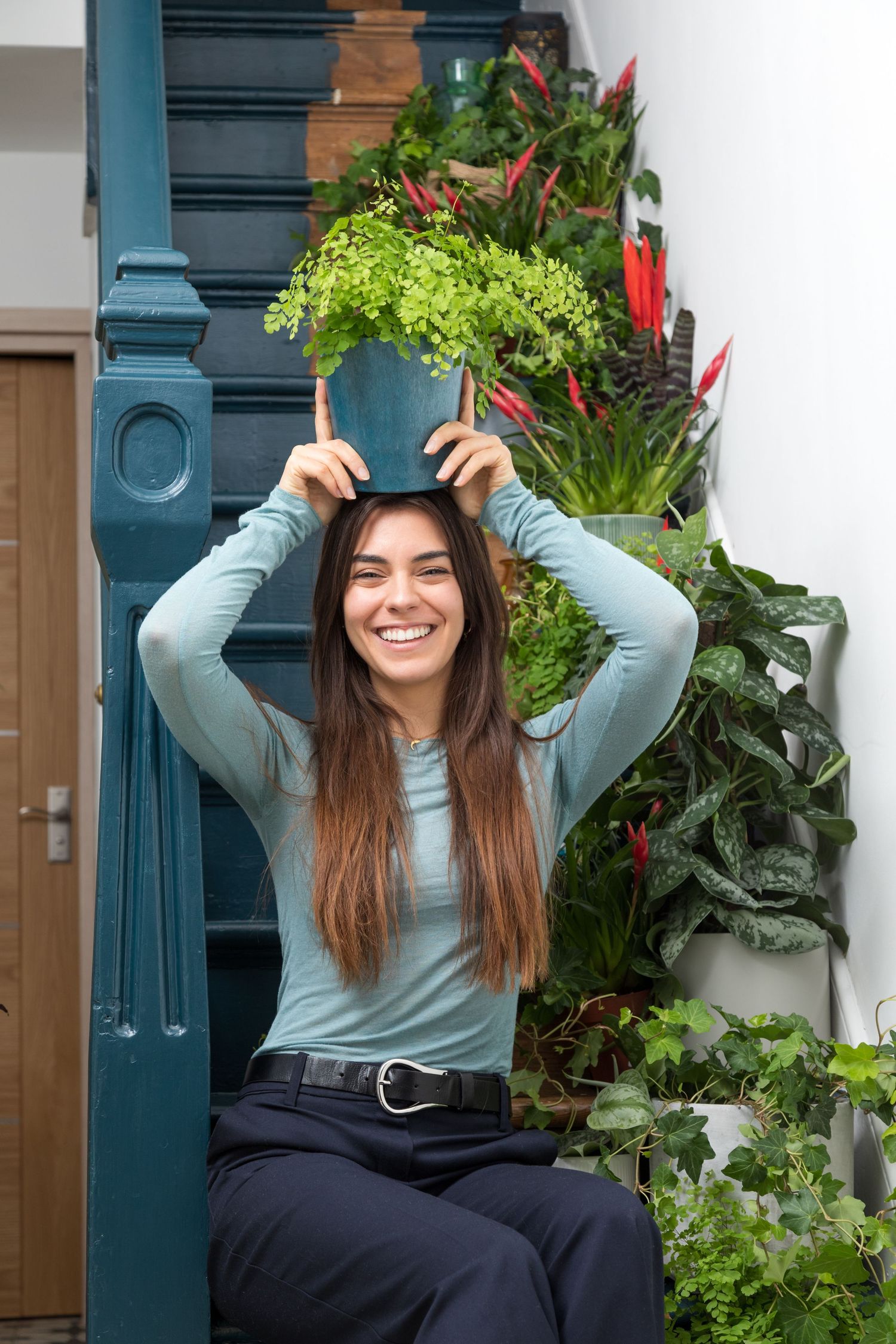 Professional personal branding portrait of a woman holding a houseplant, surrounded by lush indoor greenery in a bright botanical setting.