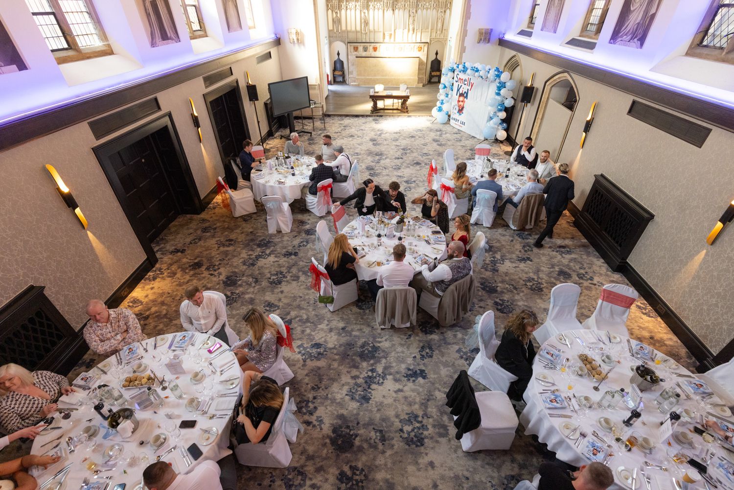 Overhead view of an elegant events venue with round tables, white linens, and floral centrepieces in a grand ballroom.