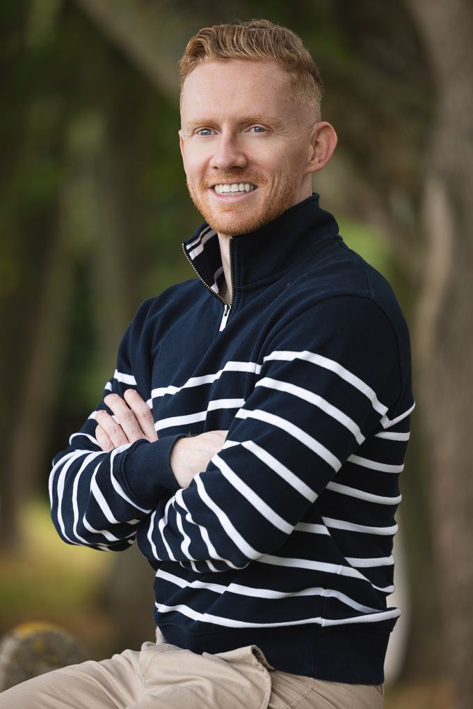 A person wearing a navy and white striped sweater poses outdoors against a natural background.
