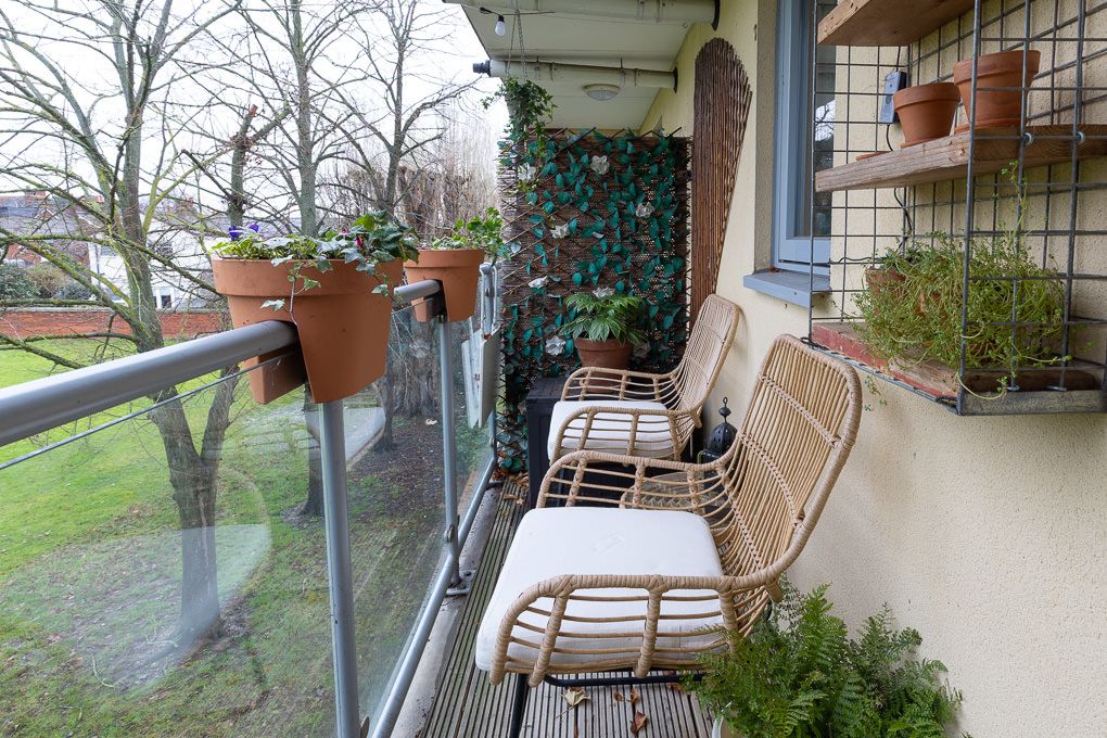Real estate photography of a cosy balcony with rattan chairs and hanging plants overlooking a peaceful outdoor landscape in Hertfordshire.