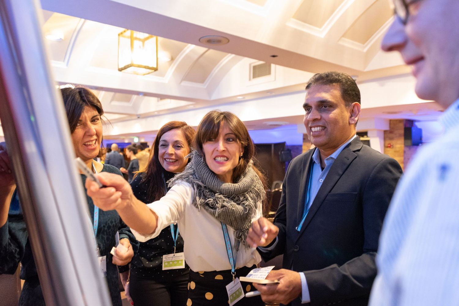 Professionals networking at a conference, smiling and discussing ideas near a presentation board in a elegant venue.