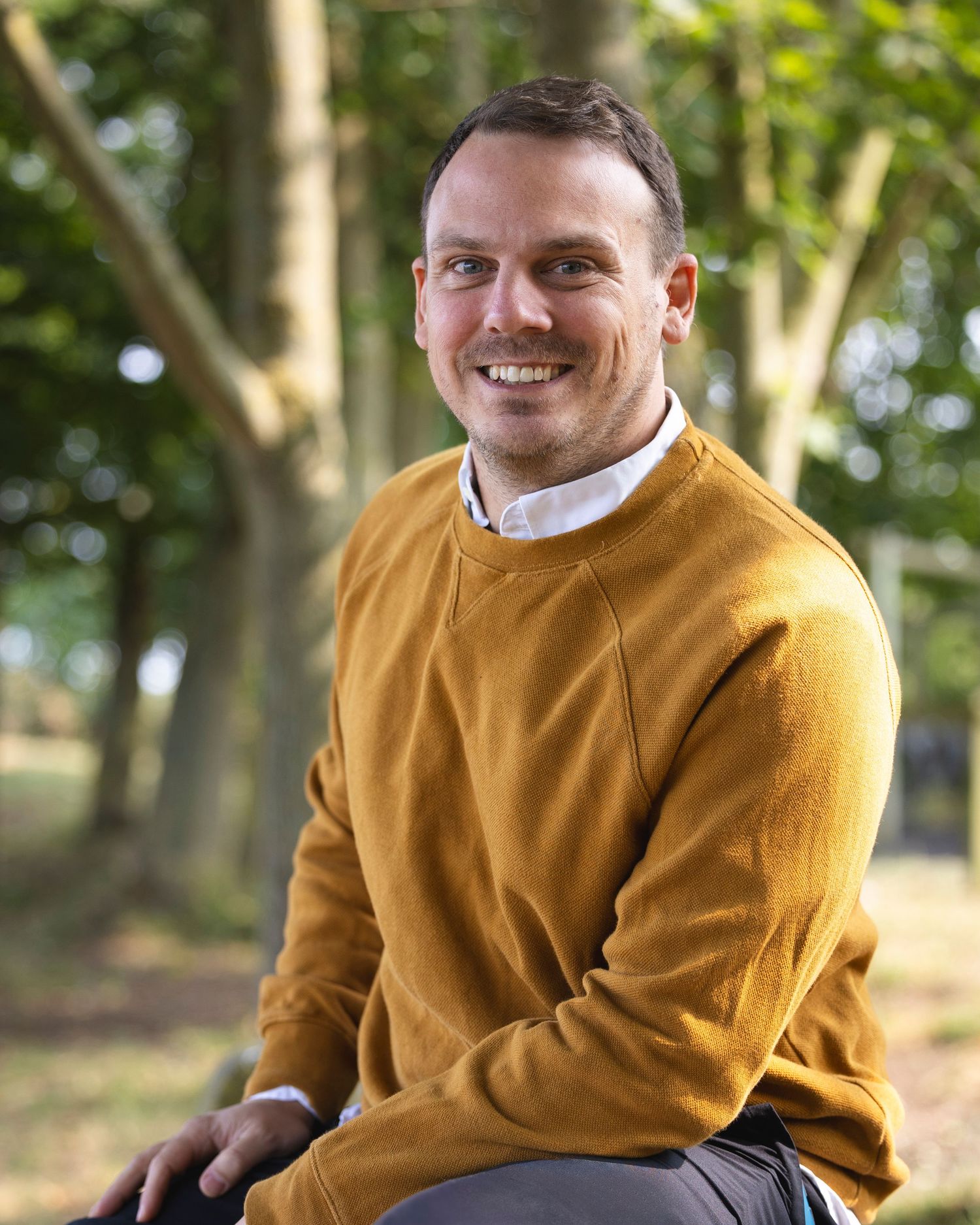 Professional outdoor portrait of man sitting in a natural park setting, photographed for personal branding and lifestyle marketing.