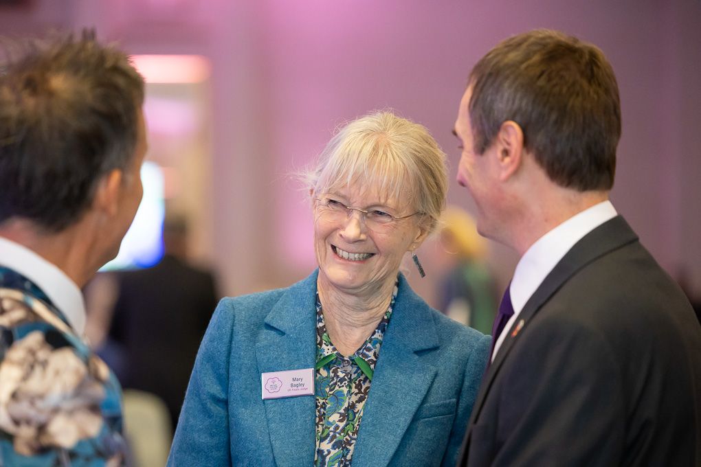 People networking and conversing at a professional business conference with a pink-tinted background.