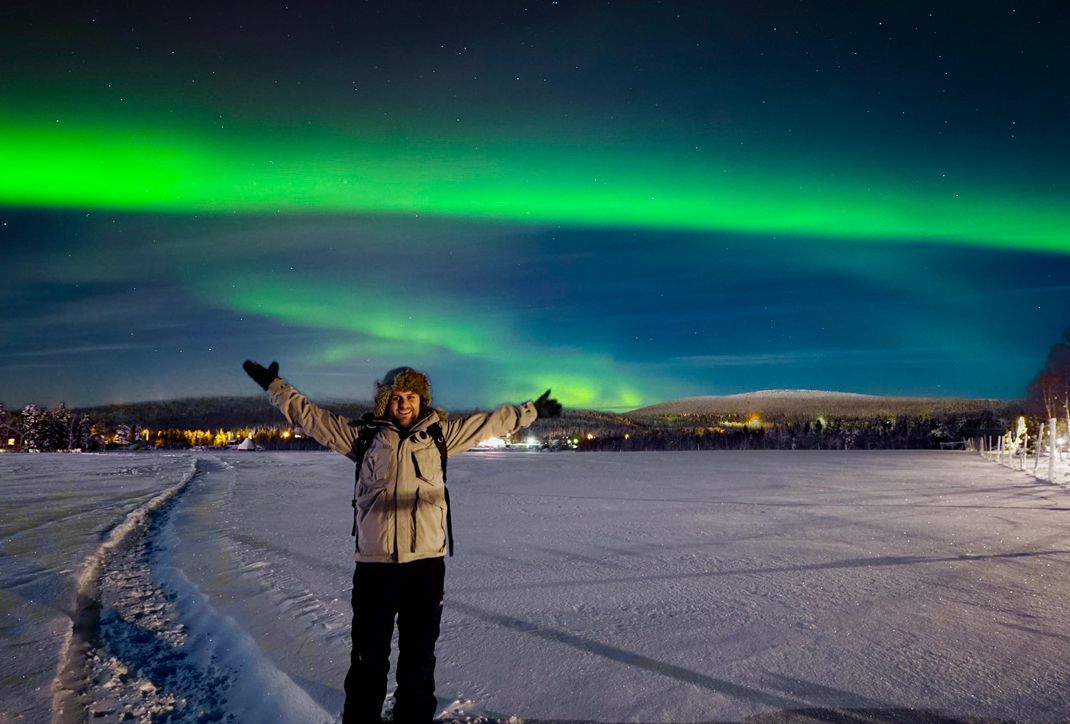 Lee Charlton standing beneath the Northern Lights in snowy Finnish Lapland.