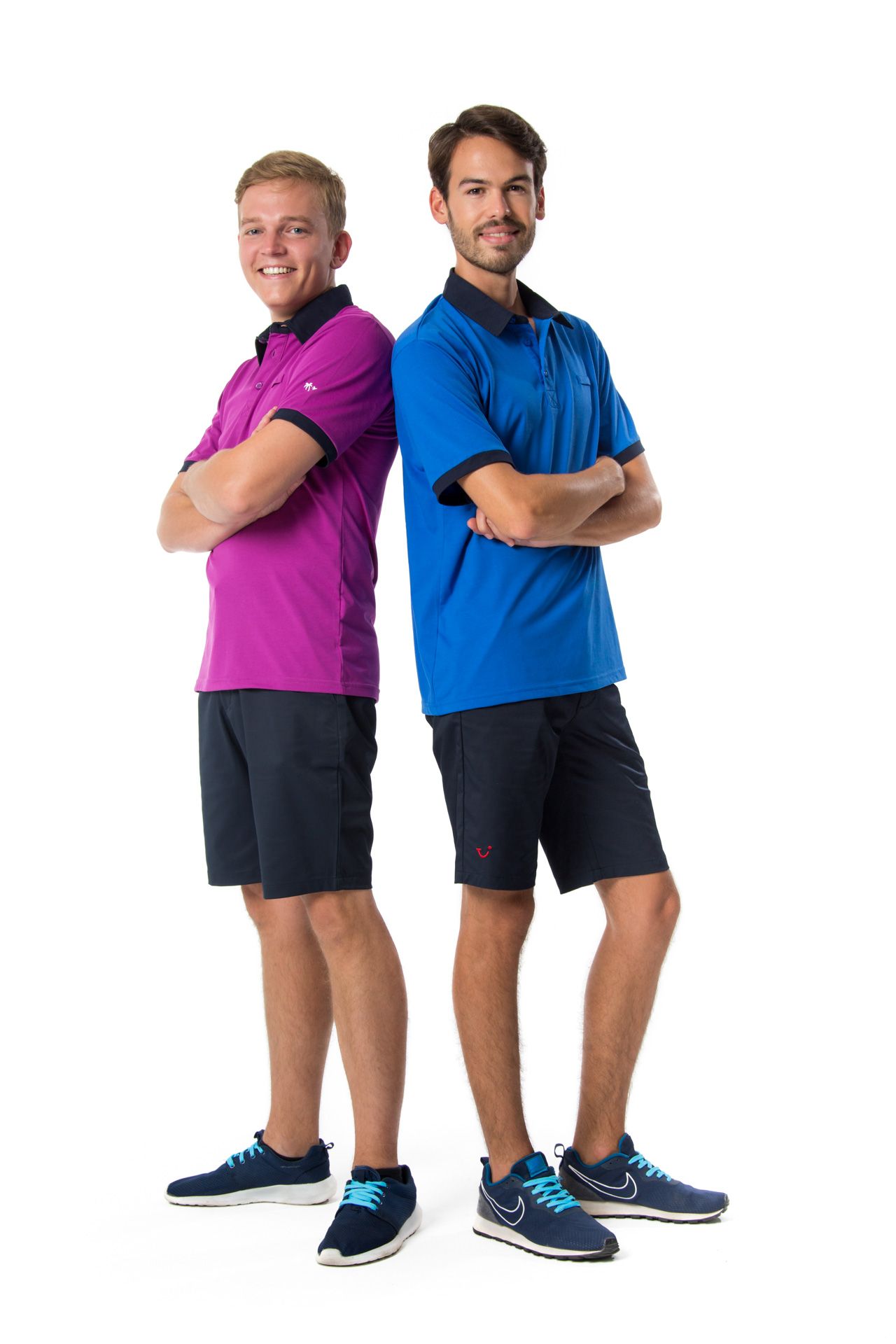 Two athletic men in polo shirts and shorts stand back-to-back with arms crossed wearing navy sneakers on white background.