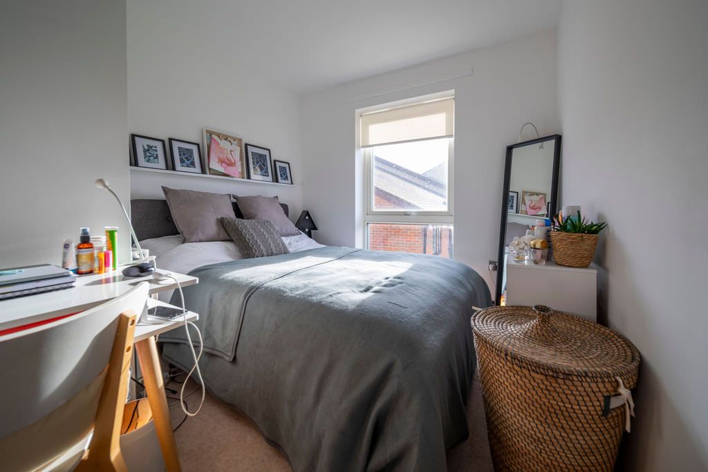Interior photography of a modern bedroom interior with grey bedding, a natural woven basket, and framed photos displayed on white walls.