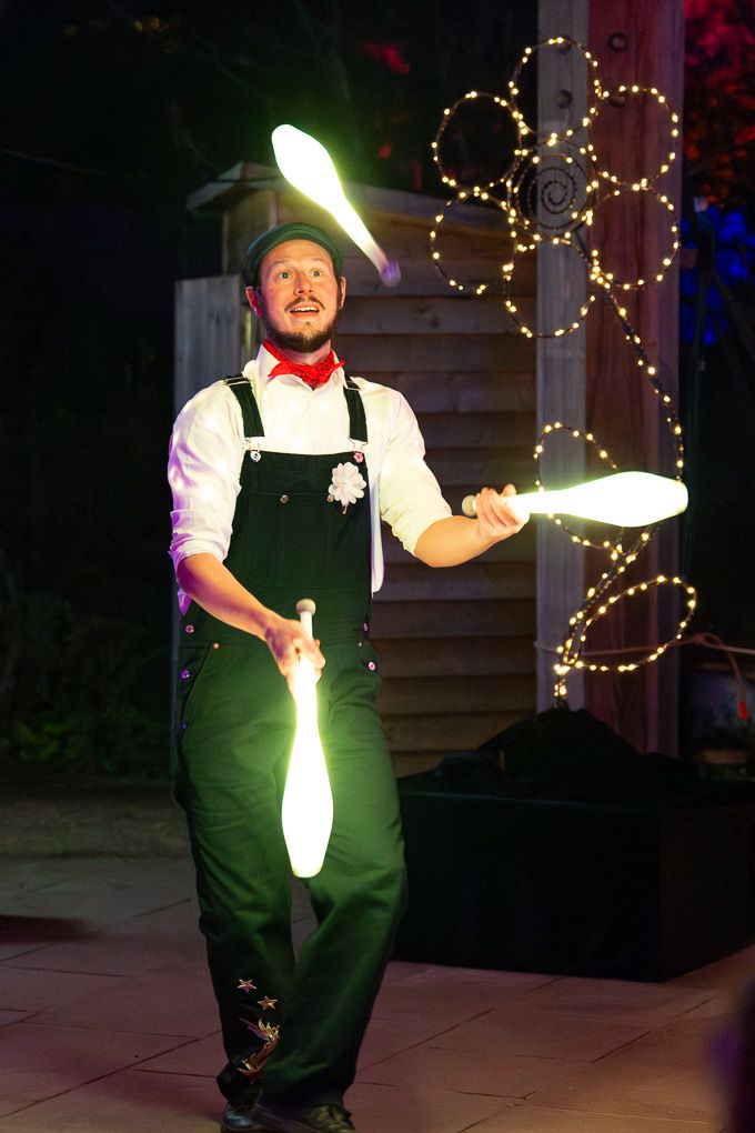 Performer juggling glowing LED pins at night during the illuminated show at Glow at RHS Bridgewater, with colourful decorative lights.