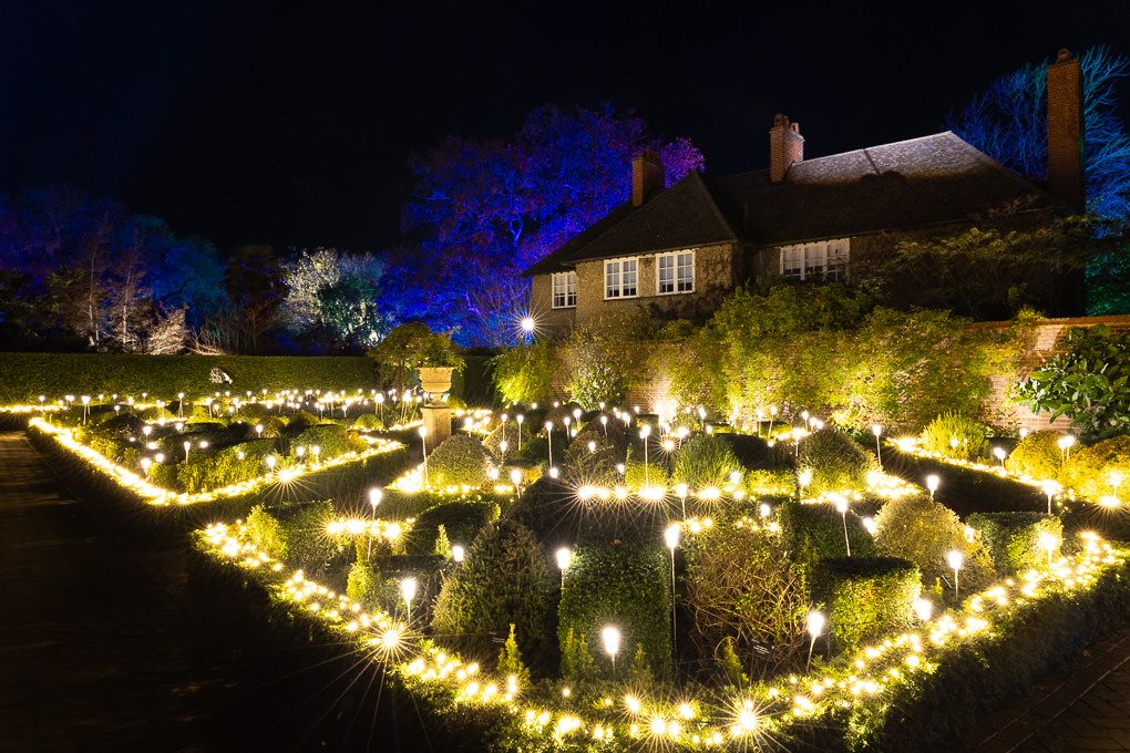 Illuminated garden pathways with warm glowing lights creating a magical nighttime scene in the Walled Garden at RHS Wisley.