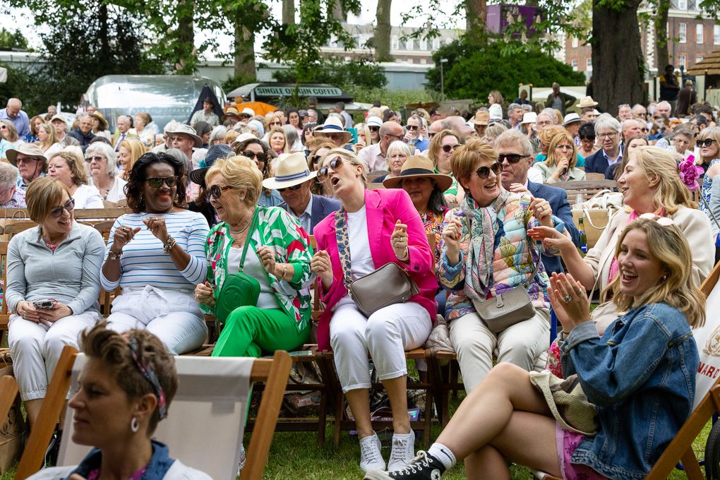 A large outdoor crowd dancing and singing along to live music performed at the RHS Chelsea Flower Show.