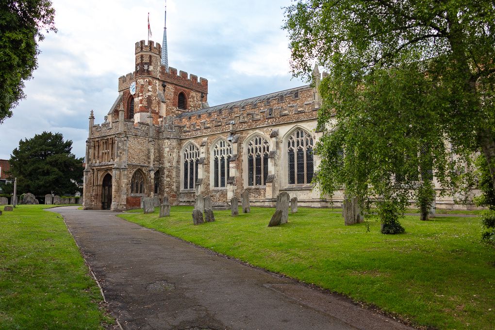 St Mary's church in Hitchin and the surrounding graveyard with a cobblestone path and green trees.