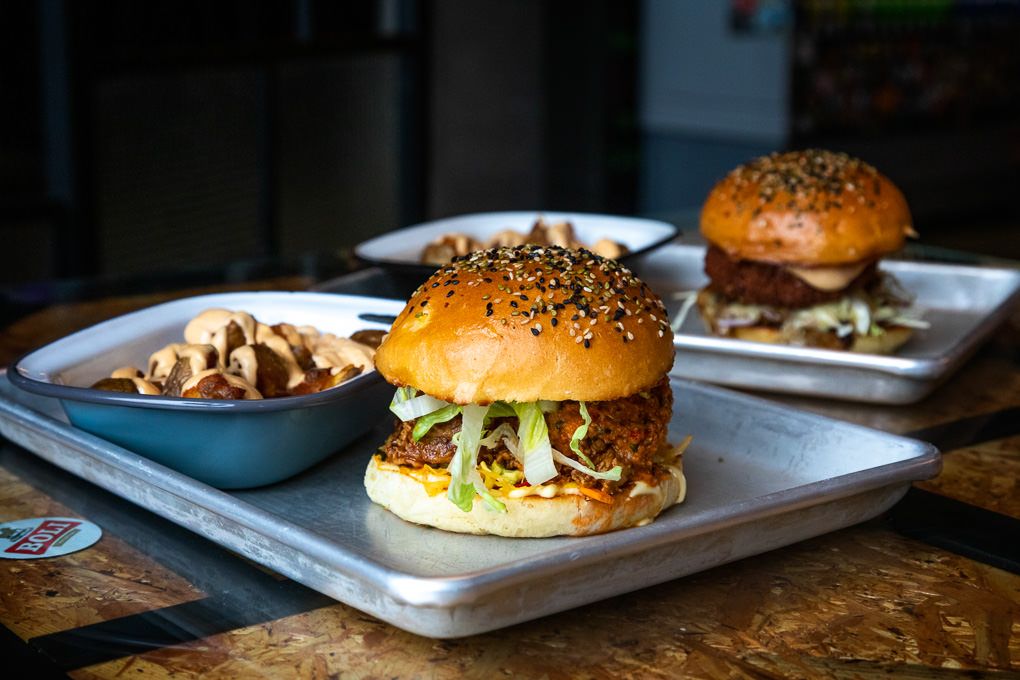 Gourmet hamburger with sesame seed bun and fresh toppings served on a white plate with side dishes at Le Kok restaurant in Iceland.