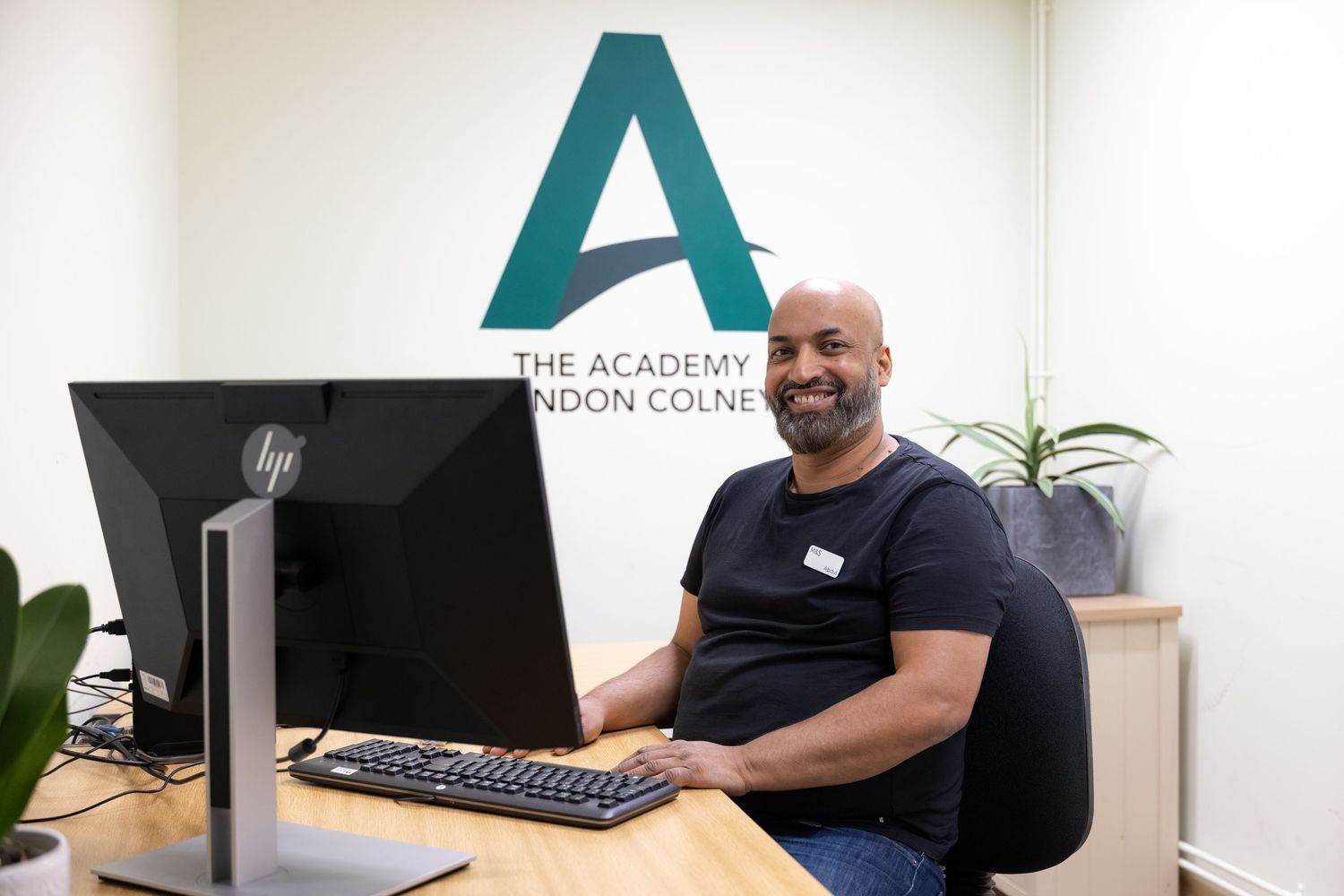 Corporate office photography of an employee smiling at his desk at The Academy in London Colney.